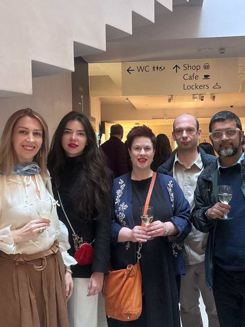 Group of five conference delegates smiling and holding drinks in a museum foyer.