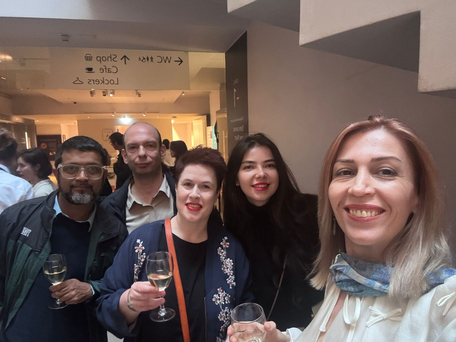 Five smiling delegates taking a selfie-style photo with drinks in hand.